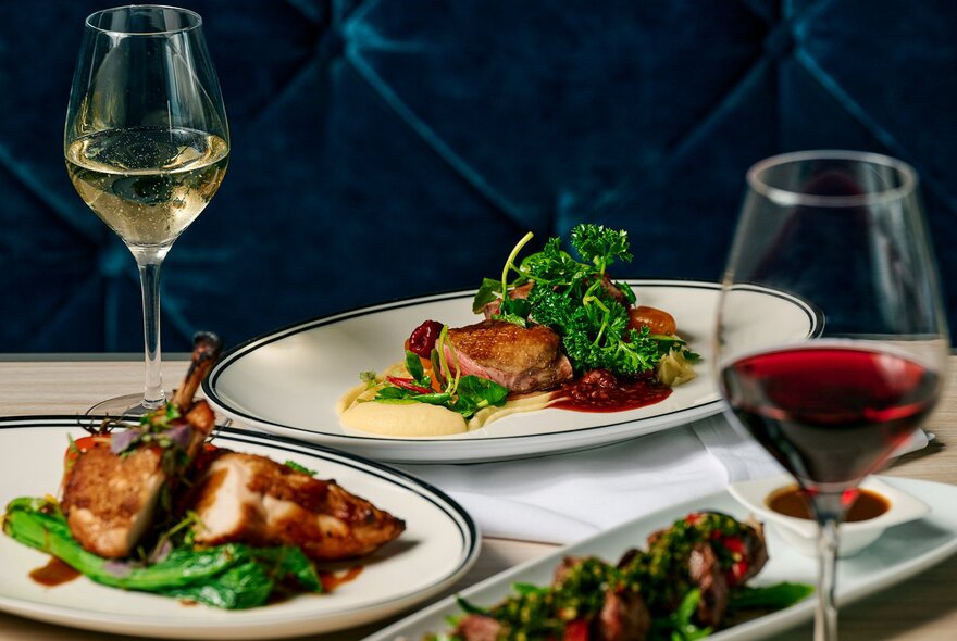 Plates of roast meat and vegetables with glasses of wine.