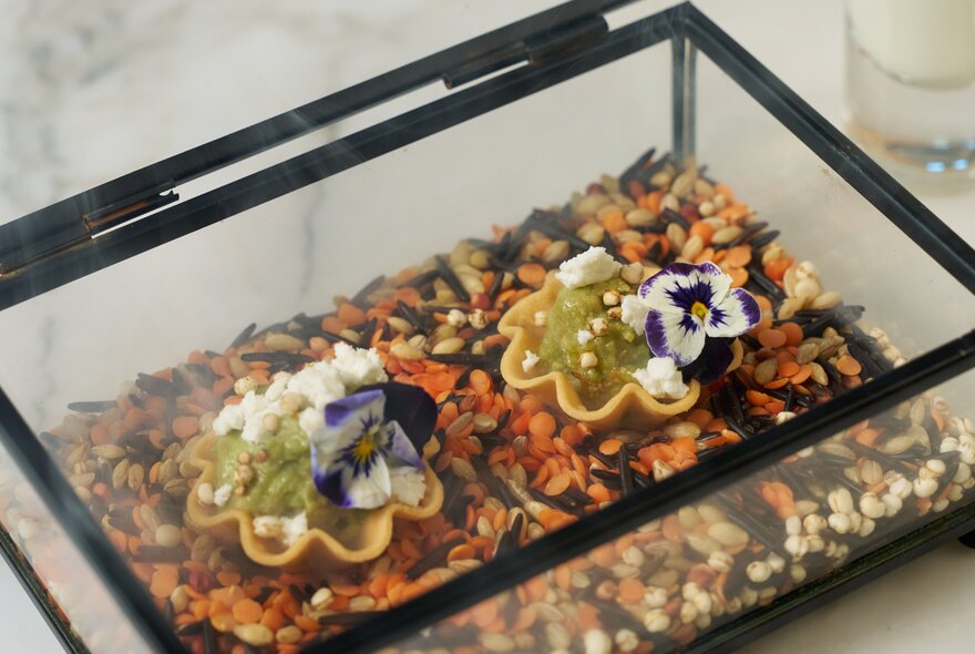Two flower-bedecked tarts resting in a glass display case.