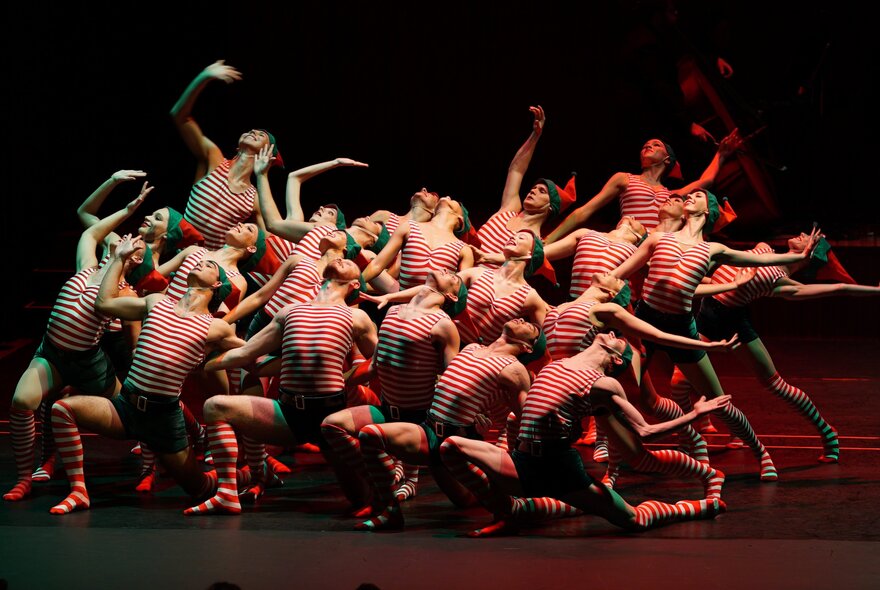 Rows of dancers wearing striped red and white tops, performing in a group on stage.