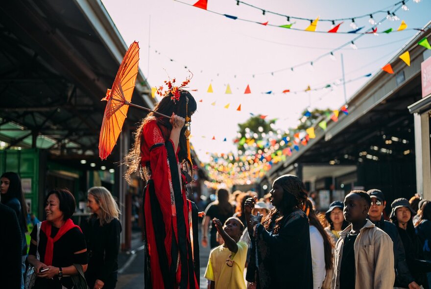 Crowds in the Queen Victoria Market lanes with performers and flags.