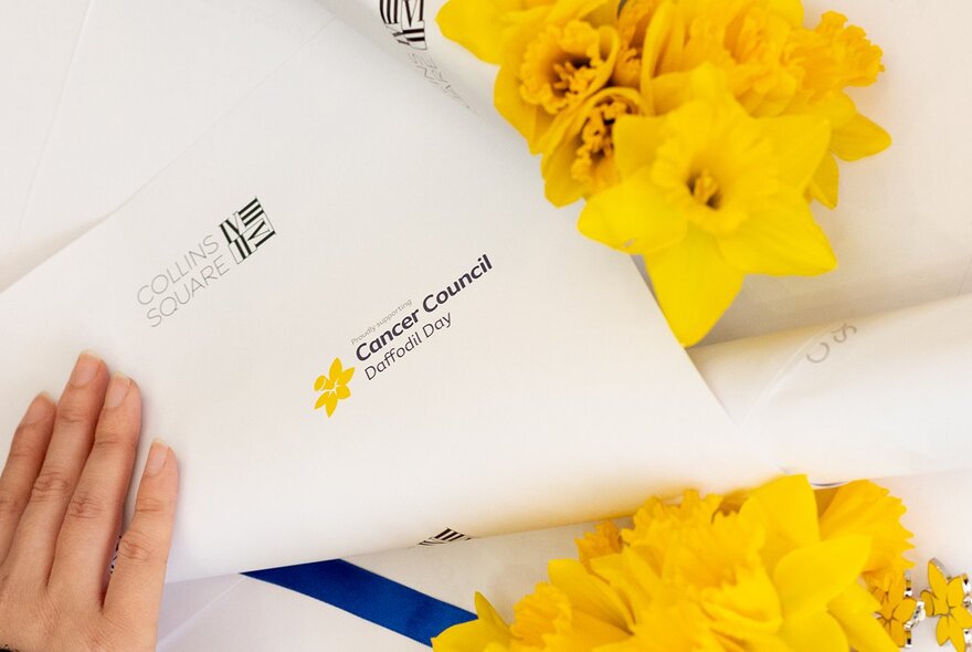 A hand wrapping a bunch of yellow daffodils in white paper.
