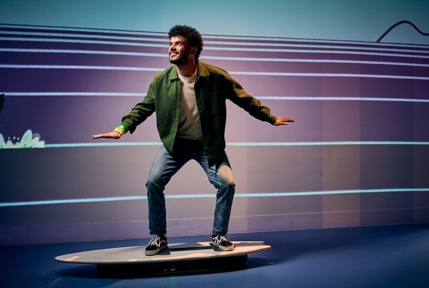 A man surfing on a fake surfboard in a room with a wave mural on the wall.