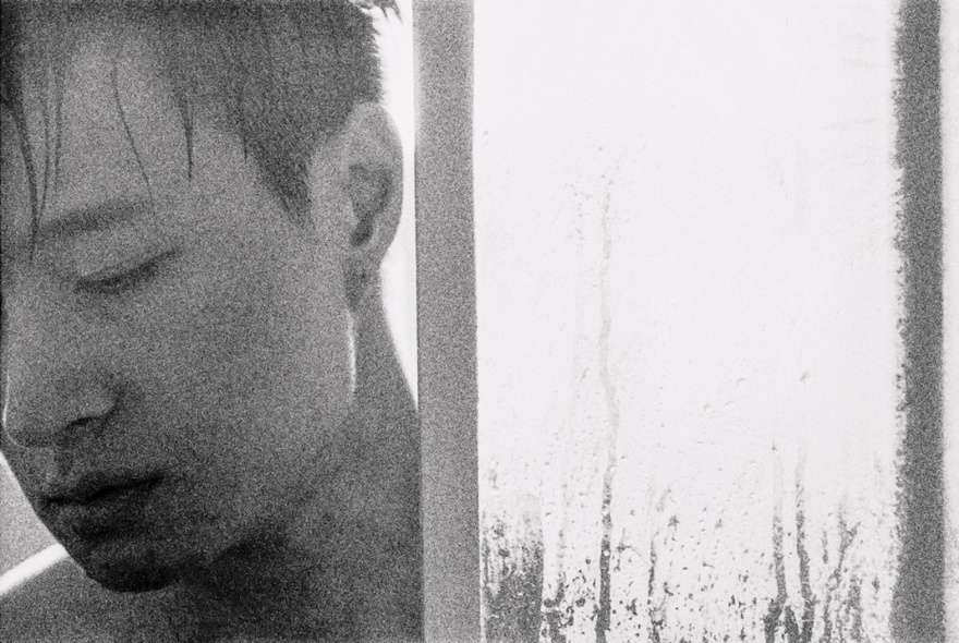 Self portrait of an artist in black and white, looking down from behind a glass shower frame.