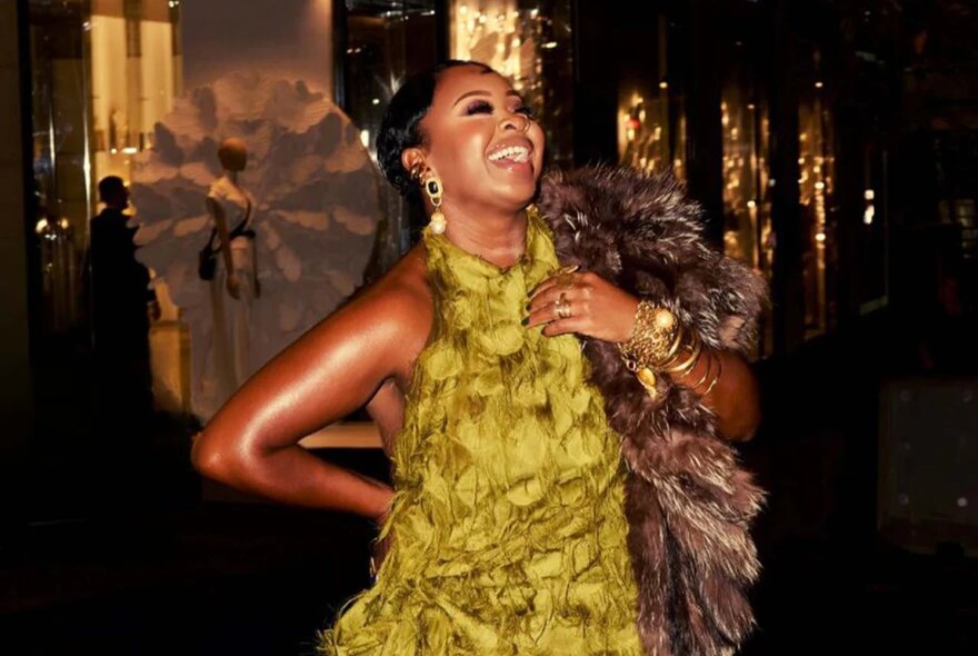 A fashion model tilting her head back and laughing, wearing a halter neck gold coloured ruffled dress.