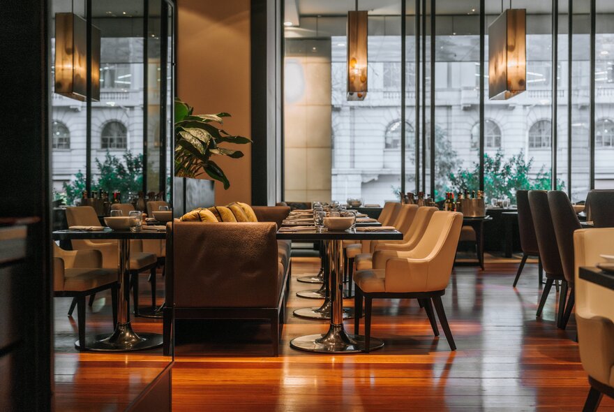 The restaurant interior of Collins Kitchen, featuring polished wooden floors, modern tables with beige upholstered chairs, and large windows overlooking a city street.
