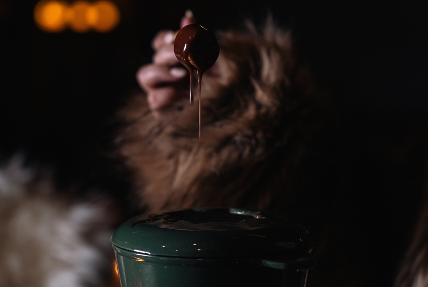 A hand dipping a marshmallow into a chocolate fondue.