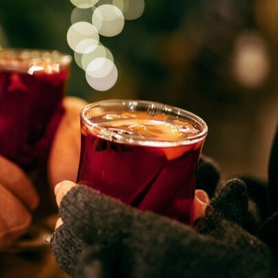 Two sets of gloved hands holding glasses of hot mulled wine.