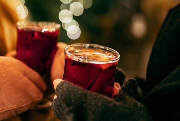 Two sets of gloved hands holding glasses of hot mulled wine.