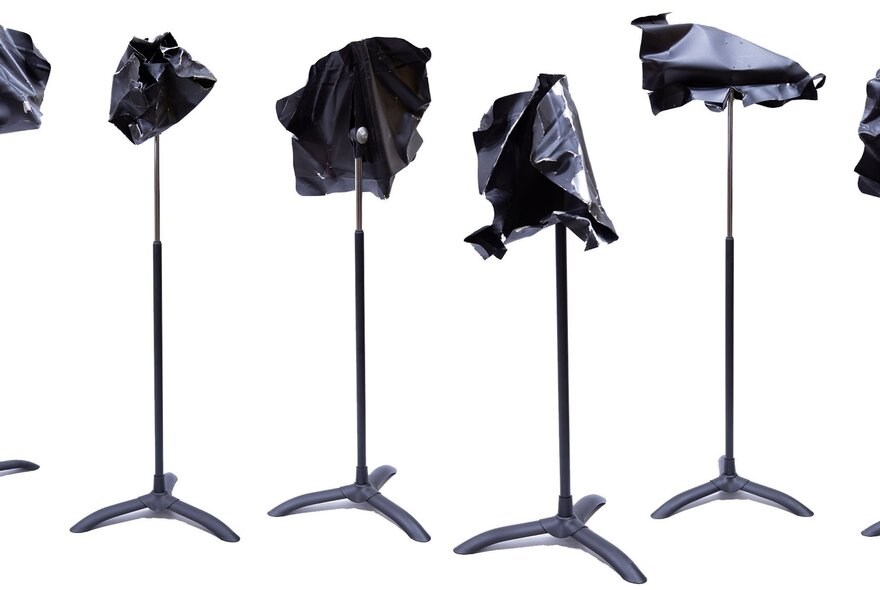 Five percussive items of twisted metal shapes secured to the top of a music stand, against a white background.