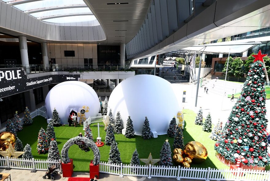 A Christmas scene with a giant tree and smaller trees and white igloos.