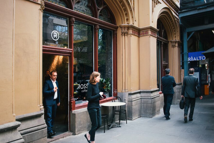 Heritage sandstone coloured exterior of Rosso Espresso Bar, with large glass windows, and two people exiting the cafe onto the street.