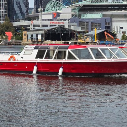 A red and white tour boat on the Yarra River, with buildings on the riverbank behind it.