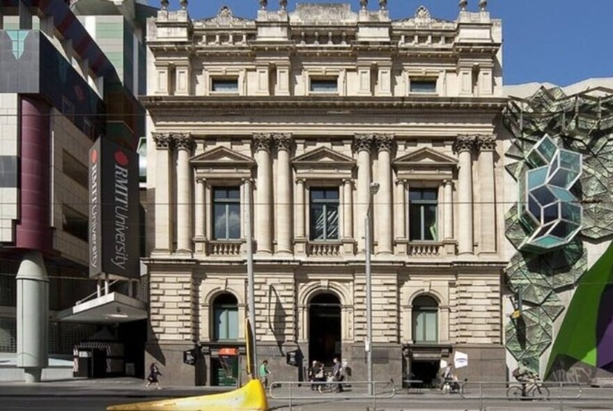 Exterior of an old building with columns and a modern geometric extension. 