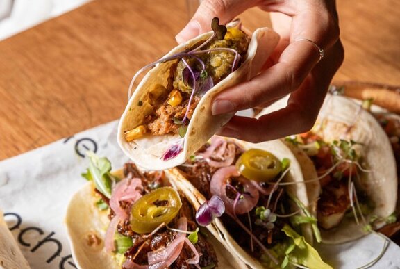 A hand selecting a filled soft taco from a plate of tacos.