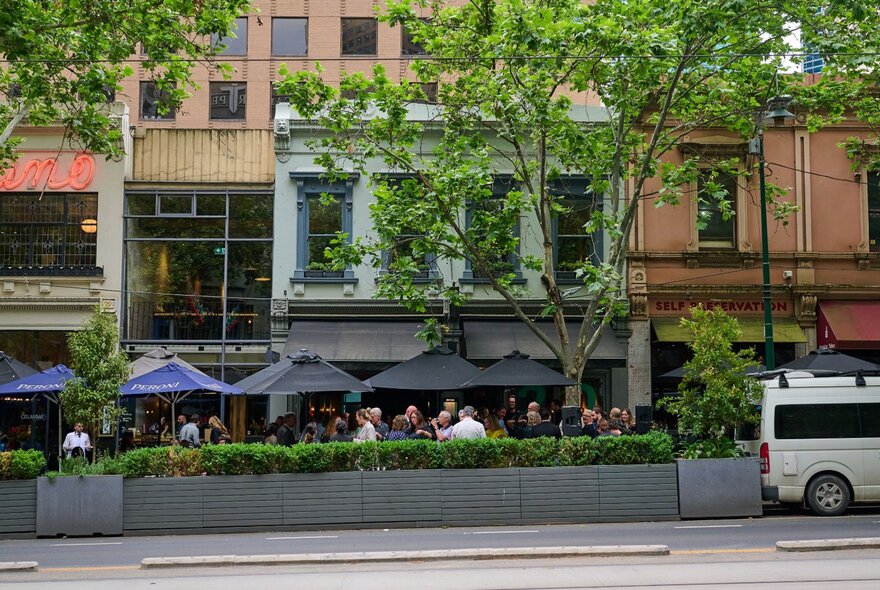Exterior of Bottega restaurant on Bourke St showing surrounding buildings, and patrons dining on the footpath.