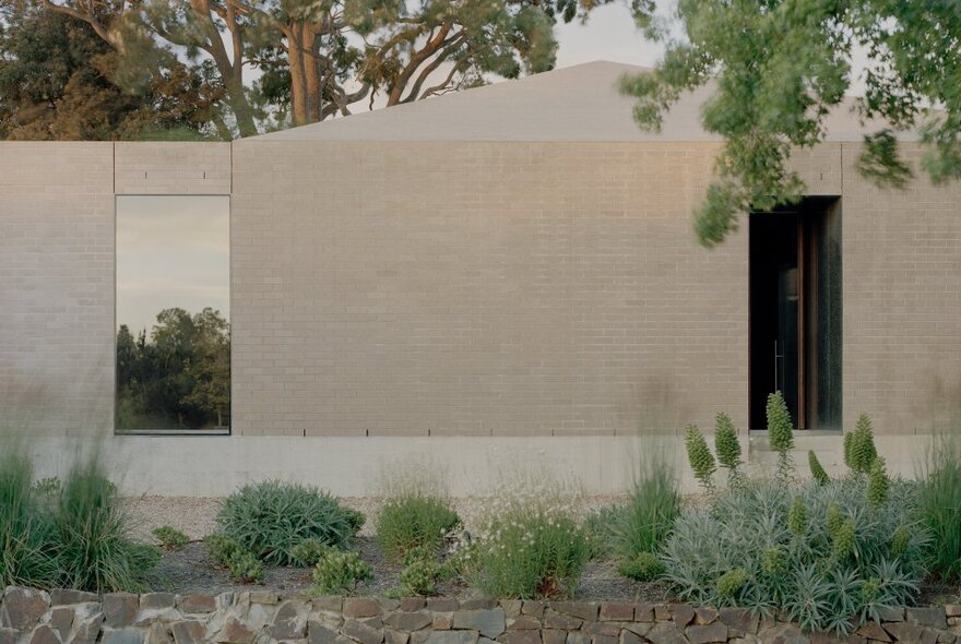 A pale exterior wall with an open doorway and succulent garden, trees visible behind. 