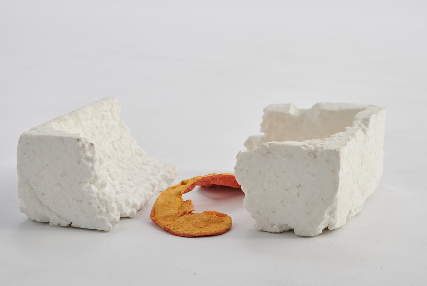 An art object comprising two pieces of white stone with an orange peel resting on the ground between them.