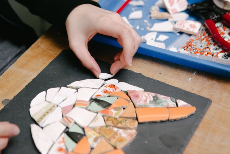 Hands making a mosaic picture of a ginger cat face. 