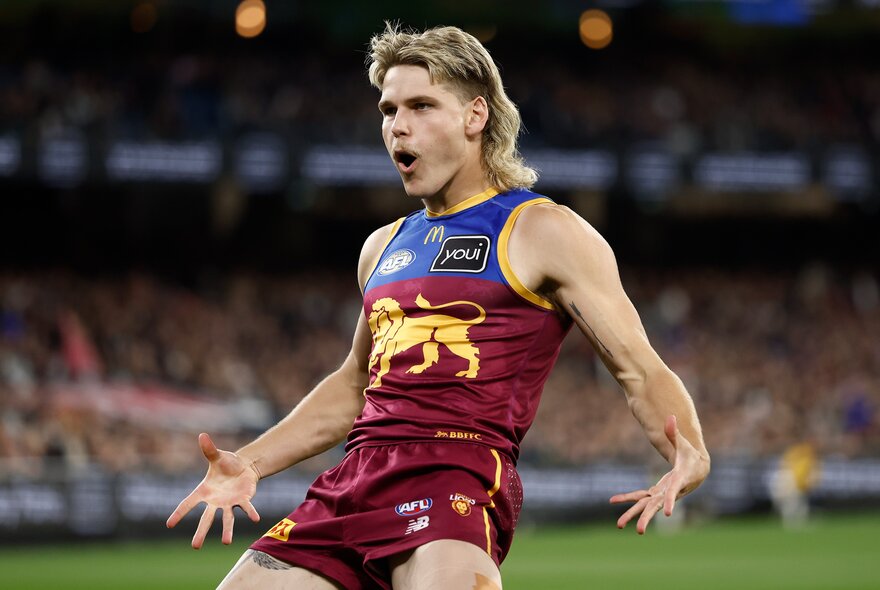 A Brisbane Lions AFL player with arms out, leaning backwards and looking with mouth open. 