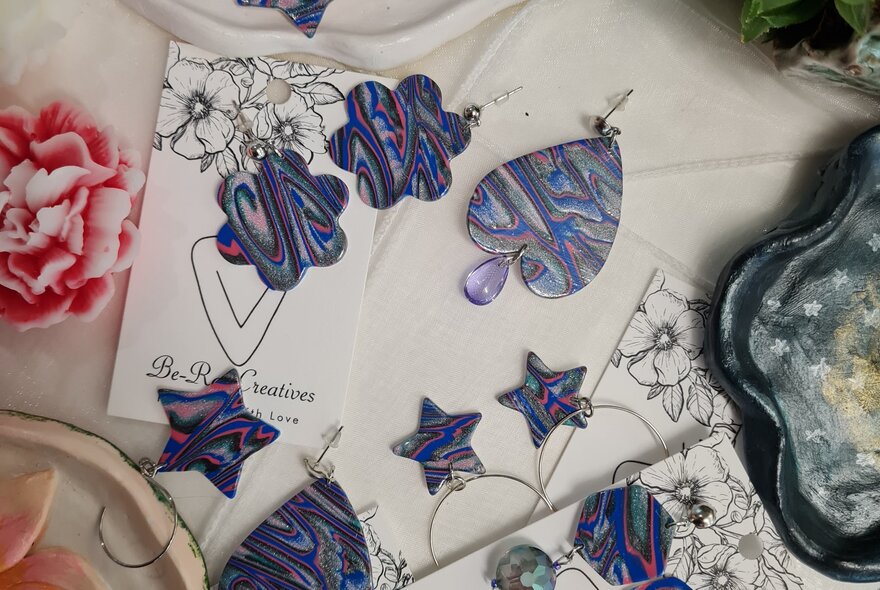 Polymer clay earrings in swirly shades of blue against  a floral material background.