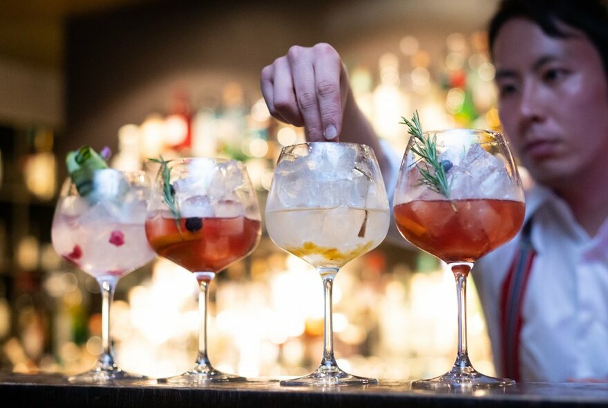 Bartender adding garnishes to four cocktails on a bar counter.