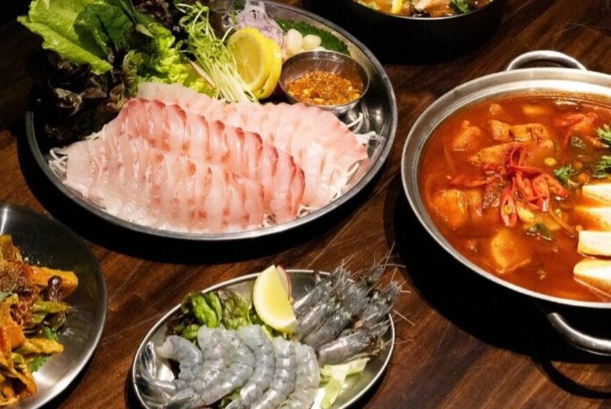 Platters of sashimi, a fish stew and other fish and crustaceans, on a restaurant table.