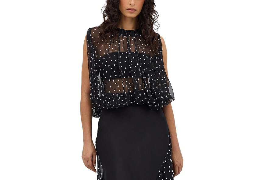 A model wearing a sheer spotty black and white top over a bra and skirt.