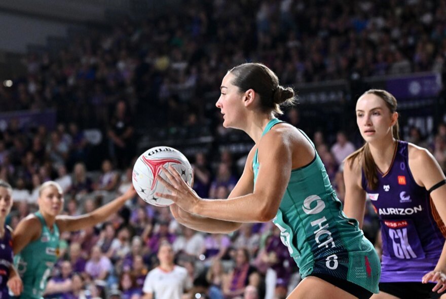 Women's netballers during a game, one player holding the ball while others surround her.