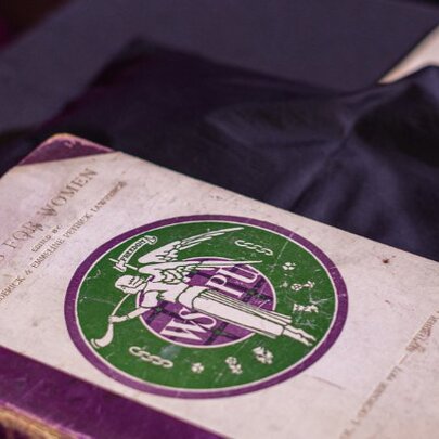 A vintage copy of a book titled, Votes For Women, from the WSPU, resting on a blue silk cloth.