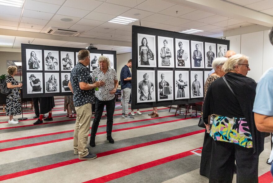 People in a gallery space looking at portraits displayed on wall dividers.