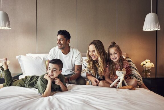 A family sitting on a hotel bed laughing. 