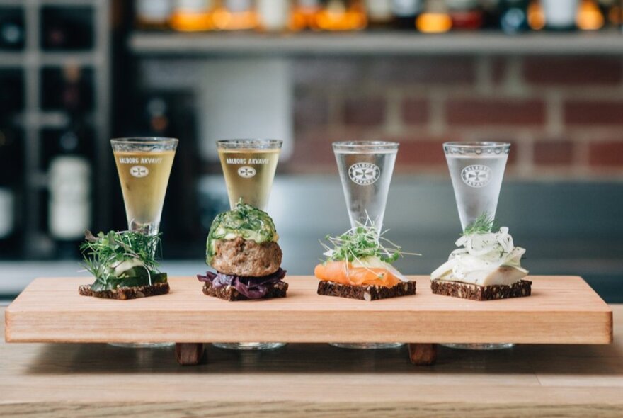 Lineup of drinks and open sandwiches on a wooden board.