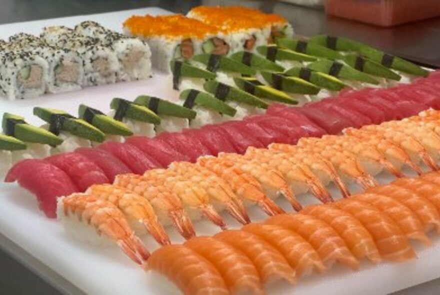 A colourful array of salmon, prawn, tuna and avocado sushi with california rolls on a white serving platter.