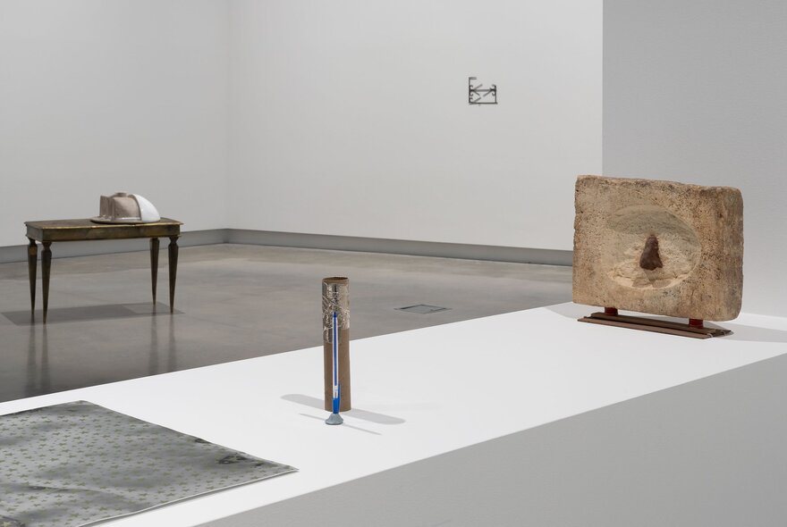 A large white room in a gallery, with an installation view of varied artworks on display.