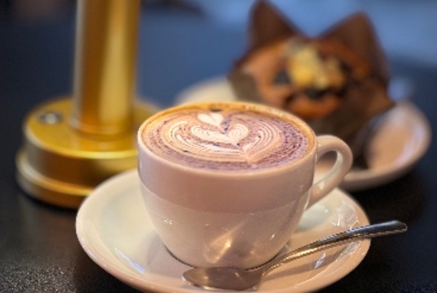 A cappuccino in a cup, a muffin in the background.