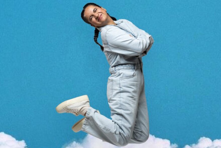 Comedian Urooj Ashfaq jumping in a straight-jacket against a sky background with clouds at the bottom. 