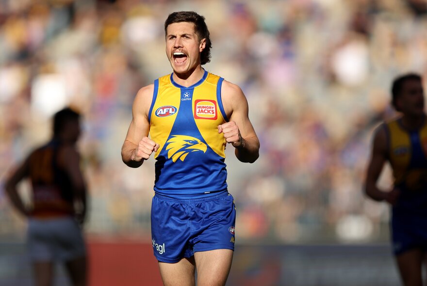 A West Coast Eagles AFL football player on the field during a match with his fists pumped by his side, cheering himself on.