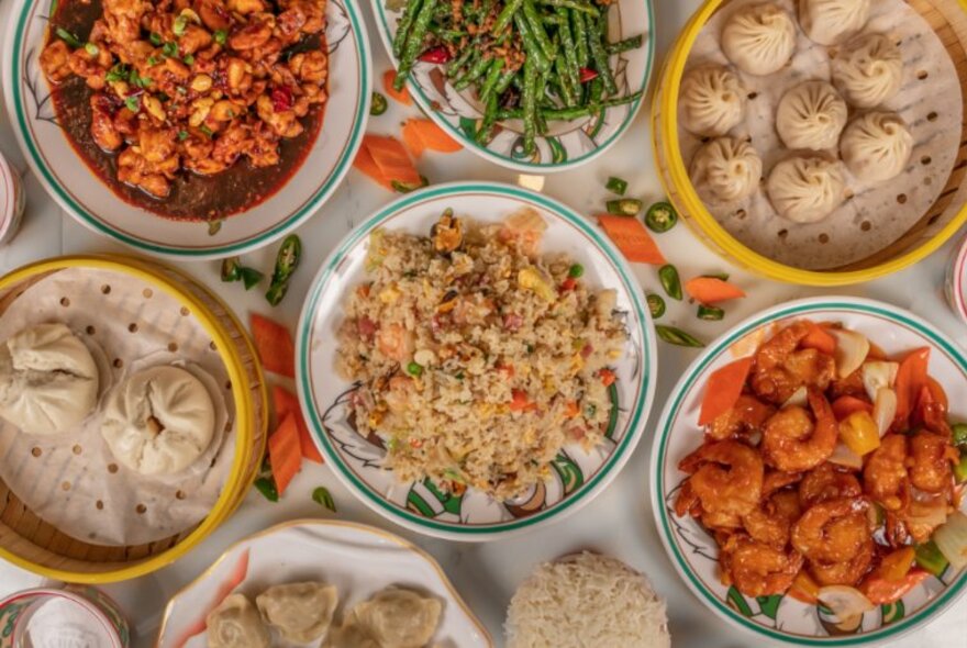 Looking down at a selection of plates of Chinese food on a café table including dumplings, fried rice, prawns, and green beans.