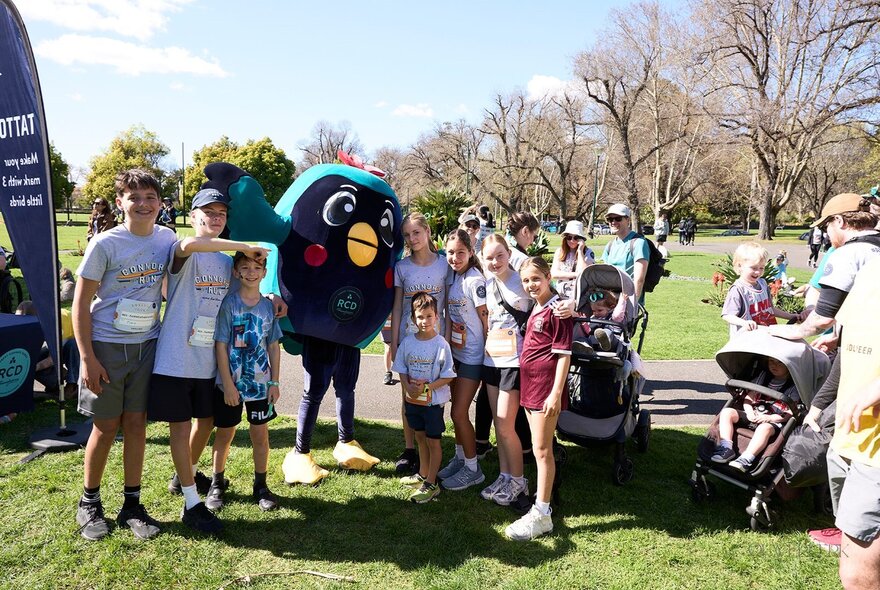 A group of people in running gear having completed a fun run, posing outdoors in gardens with a mascot.