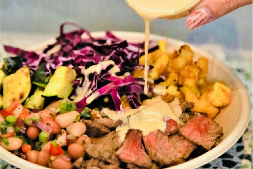 Sauce being poured on a meal that includes beans and shredded cabbage..