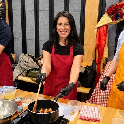 Cooking workshop participants wearing black gloves while working at stovetop workbenches with ingredients and utensils.