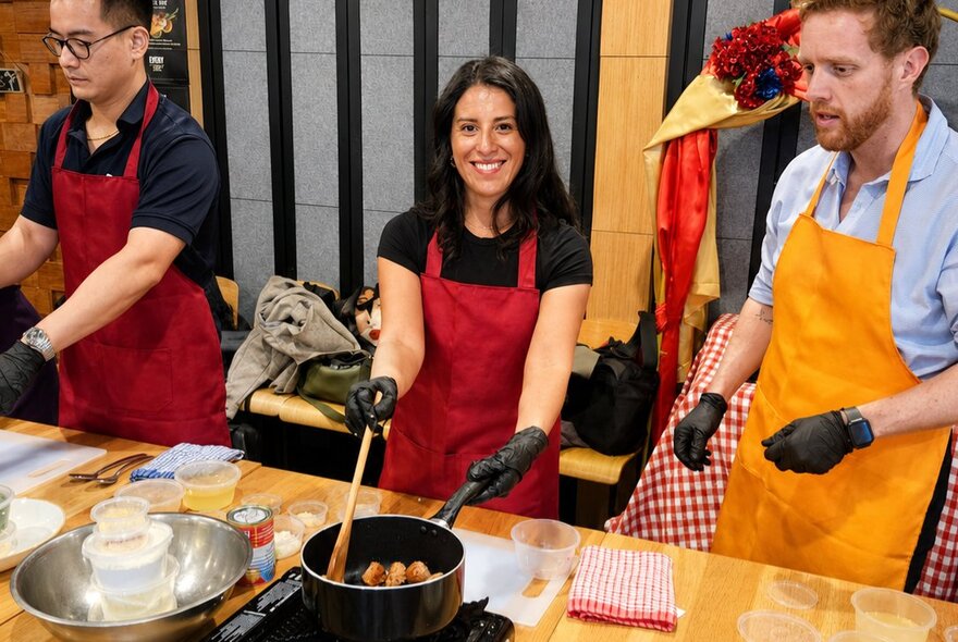 Cooking workshop participants wearing black gloves while working at stovetop workbenches with ingredients and utensils.