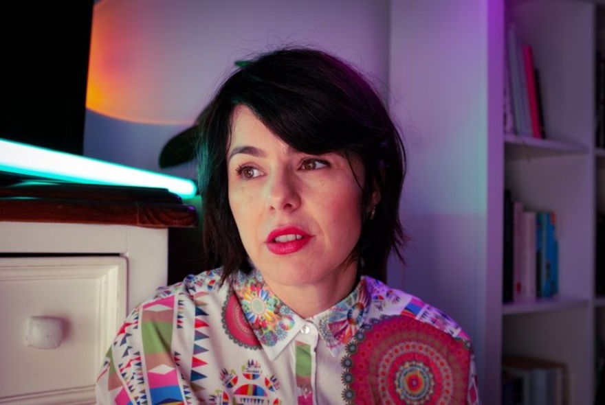 Kat Nelligan wearing a patterned shirt, in a small room looking sideways.