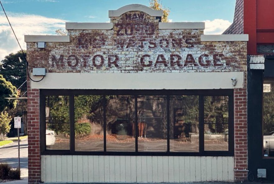 Old garage with mirrored windows and faded signage on pediment.
