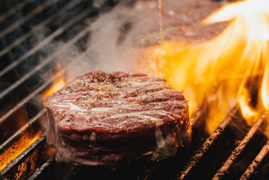 A wagyu beef steak being seared on a flame-grill.