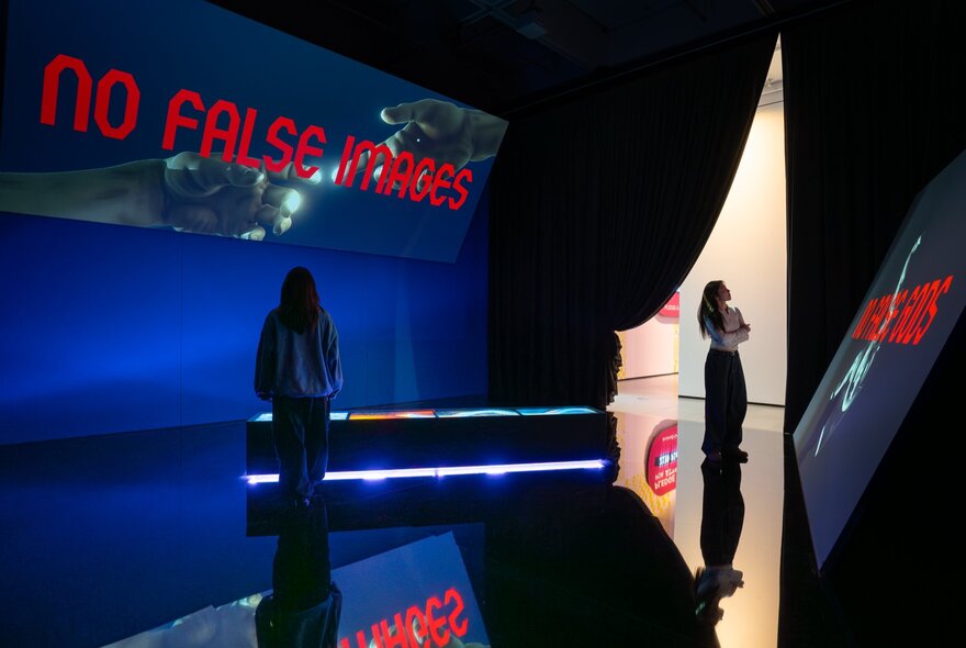 Two people in a darkened gallery space with red writing projected onto the wall.