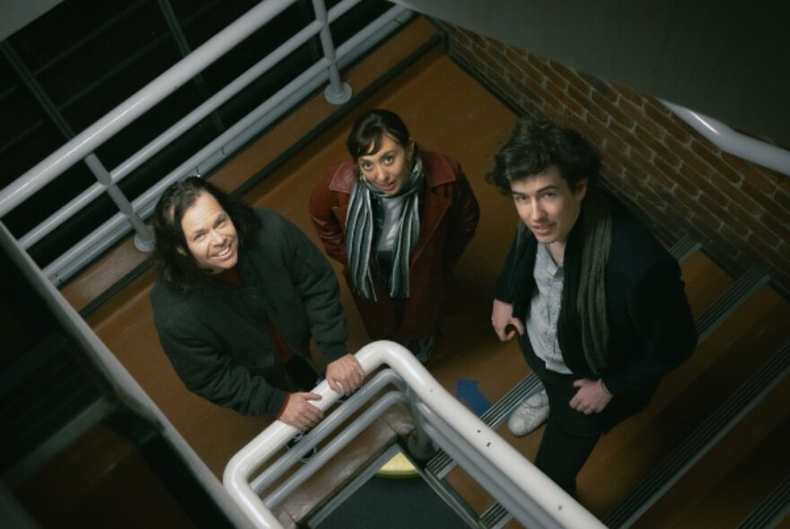 Three people standing in a stairwell and looking up.