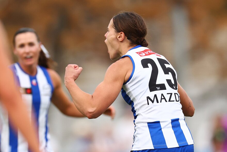 Players from the North Melbourne Kangaroos celebrating on field during an AFLW match.