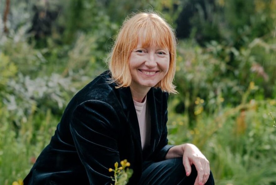 Horticulturist and author Jac Semmler,smiling and posed crouched outdoors in a garden.