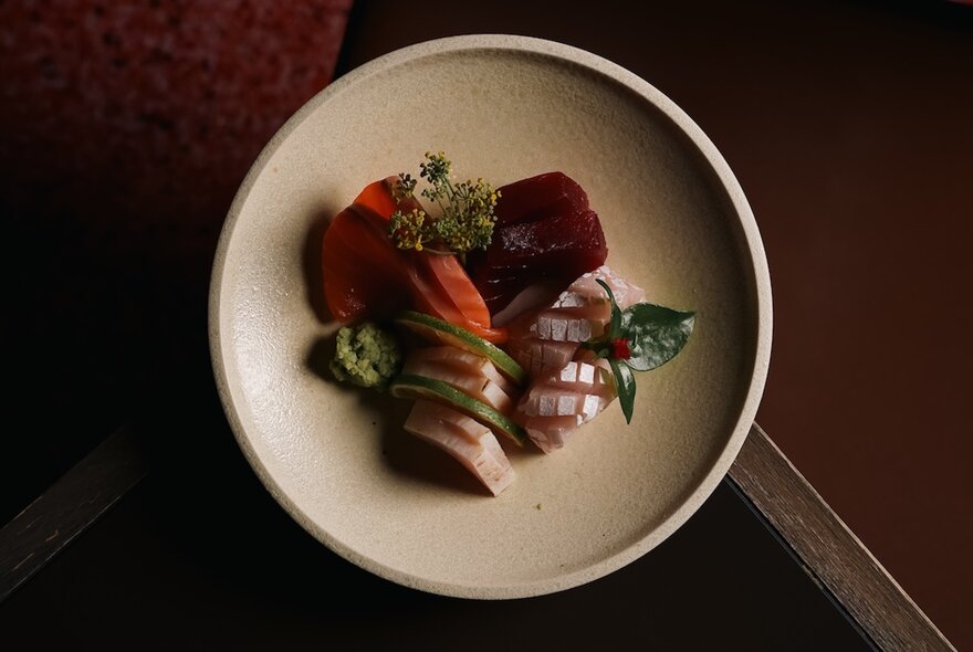Top down view of sashimi carefully arranged on a pale ceramic plate on a restaurant table.